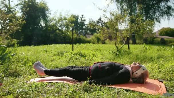 Yaşlı bir kadın bir yoga minderine uzanır ve beden eğitimi yle meşgulolur. — Stok video