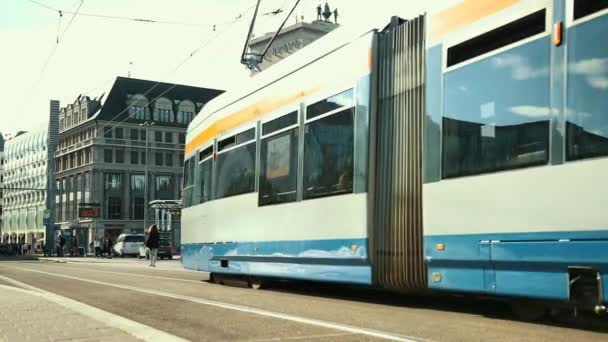 Die Straßenbahn fährt durch die Stadt, Menschen überqueren die Straße. — Stockvideo