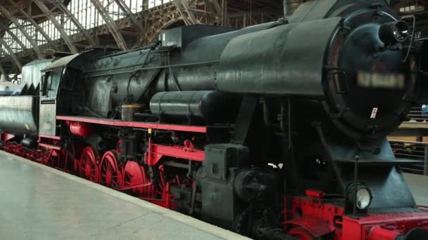 Η βαριά βιομηχανική ατμομηχανή ατμού με κόκκινο και μαύρο τιμόνι είναι στο σιδηροδρομικό σταθμό. — Αρχείο Βίντεο