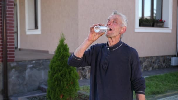 Der alte Mann, grauhaarig, faltig, trinkt aus einer durchsichtigen Glasflasche — Stockvideo