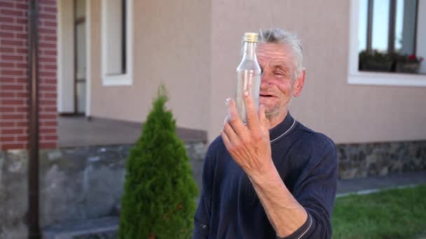 Viejo, canoso, arrugado, borracho mirando y besando una botella de vidrio transparente — Vídeo de stock