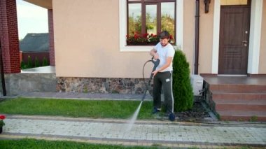 bir adam evin yakınında yüksek basınçlı su bir jet ile kaldırım yıkar