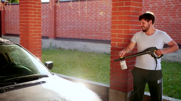 El hombre lava el coche. lavado con chorro de agua de alta presión, el aerosol se dispersa a los lados — Vídeos de Stock