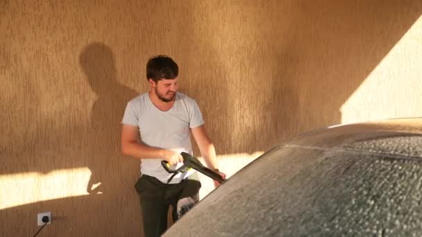 Человек моет машину. мыть струей воды высокого давления, спрей разбросан по сторонам — стоковое видео