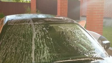 beyaz bir t-shirt giymiş genç bir adam, sabun ve sarı bir sünger araba ile yıkar