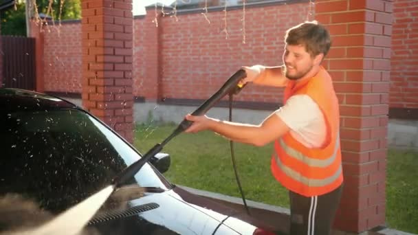 Человек моет машину, моет, используя струю воды высокого давления. Splashes spread to sides — стоковое видео