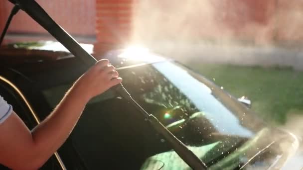 男性は、高圧ウォータージェットを使用して洗浄し、車を洗います。飛沫が側面に広がる — ストック動画