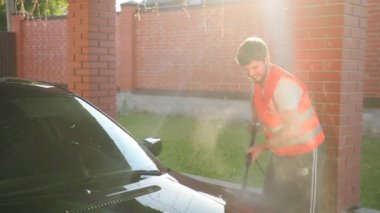 işçi yüksek basınçlı su jeti kullanarak araba yıkar, yıkar. yanlara yayılan sıçramalar
