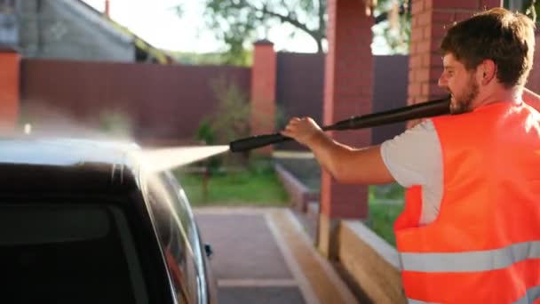 Man wast auto, wassen met behulp van hogedruk waterstraal. spatten verspreid naar zijkanten — Stockvideo