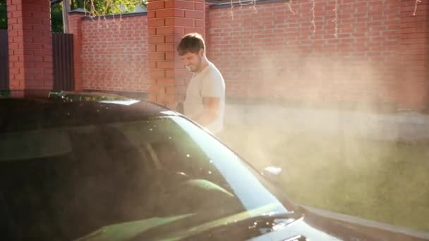 Άνθρωπος πλένει το αυτοκίνητο διεξοδικά. πλυντήριο αυτοκινήτων με νερό υψηλής πίεσης. ήλιος λάμπει — Αρχείο Βίντεο