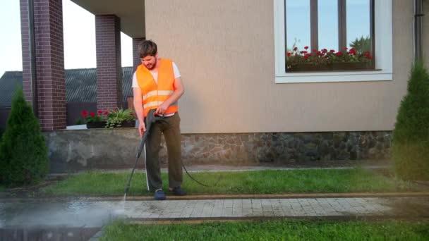 Uomo pulisce vicino casa, lava pavimentazioni, utilizza lavare con getti d'acqua ad alta pressione — Video Stock