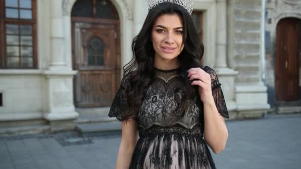 Beautiful girl dark-haired, in black dress, crown on her head, posing for camera — Stock Video