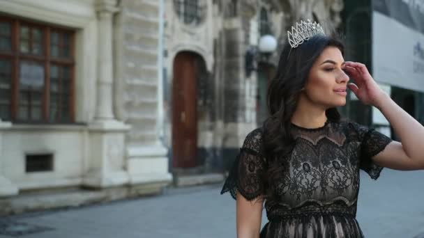Beautiful girl dark-haired, in black dress, crown on her head, posing for camera — Stock Video