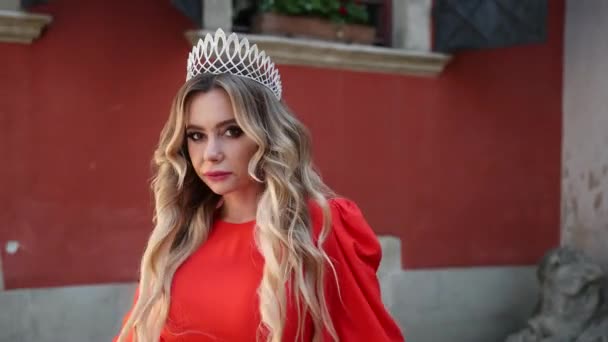 Mädchen, blond, in einem roten Kleid, eine Krone auf dem Kopf, posiert für die Kamera — Stockvideo