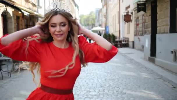 Девушка, блондинка, в красном платье, корона на голове, позирует перед камерой — стоковое видео