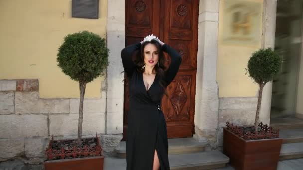 Girl, dark-haired, in black dress, with deep neckline, crown, posing for camera — Stock Video