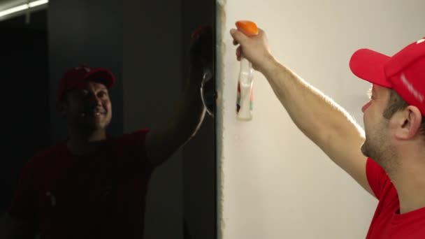 Un homme, un constructeur dans un bouchon rouge, vaporise du liquide sur des portes en verre noir — Video