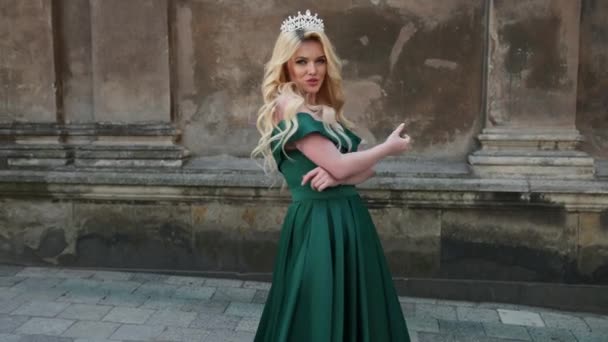 Señorita, rubia, en vestido verde con hombros desnudos, con corona, posando para cámara — Vídeo de stock