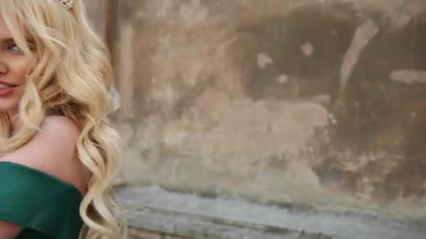 Mädchen, blond, im grünen Kleid mit nackten Schultern, mit Krone, posiert für die Kamera — Stockvideo