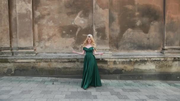 Girl, blonde, in dress with bare shoulders, with crown, posing near old building — Stock Video