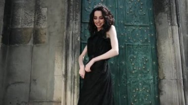 ince kız, esmer, siyah elbiseli, taçlı, poz veren, eski binanın yakınında