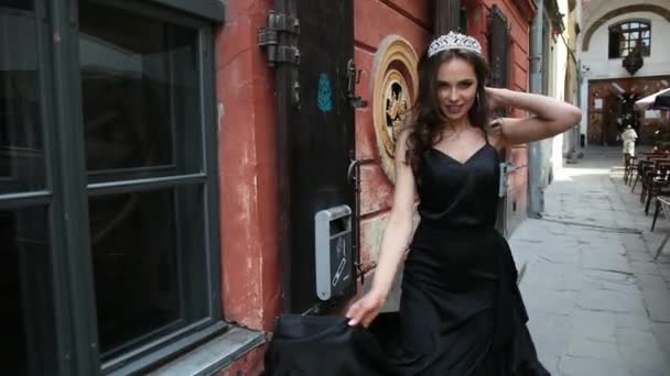 Chica, morena, en vestido negro, con el pelo largo y maquillaje brillante, corona, posando — Vídeos de Stock