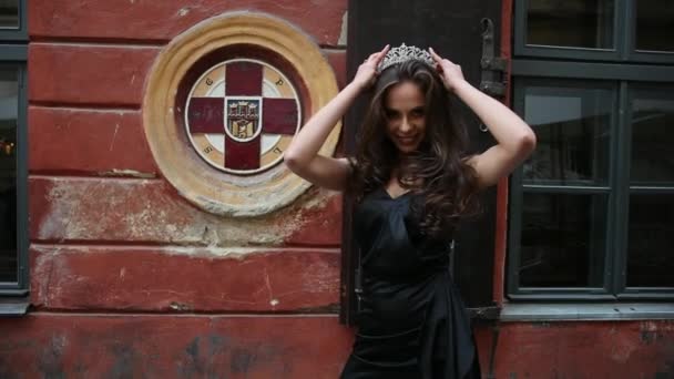 Chica, morena, en vestido negro, con el pelo largo y maquillaje brillante, corona, posando — Vídeos de Stock