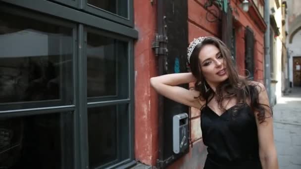 Mädchen, brünett, schwarzes Kleid, mit hellem Make-up, Krone, posiert auf der Straße — Stockvideo