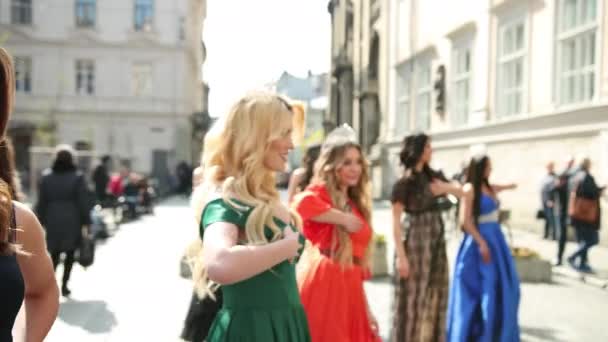 Многие красивые девушки в платьях и коронах танцуют на улице — стоковое видео