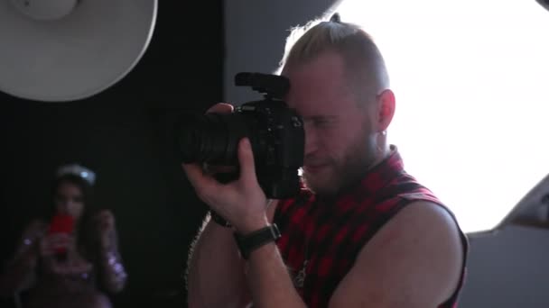 Чоловік фотограф робить фотографії з професійною камерою, в студії — стокове відео