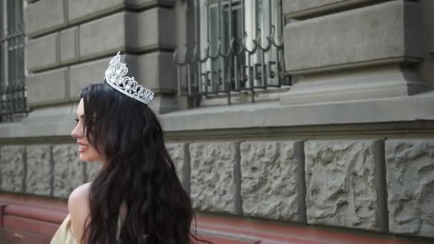 Девушка модель брюнетка в светлом платье, с короной, фотосессия на улице — стоковое видео