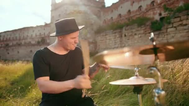 Музичний барабанщик, одягнений в чорний капелюх, грає набір барабанів і цимбалів, на вулиці — стокове відео