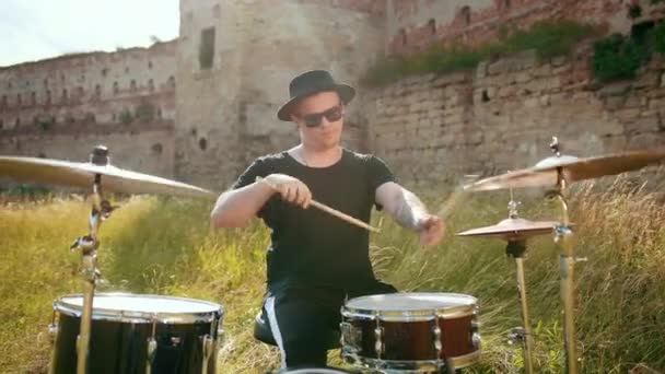 Барабанщик-музыкант, одетый в черную одежду, шляпу, играет на барабанах и тарелках — стоковое видео
