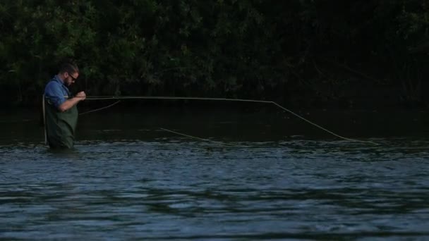 Man fiskare som innehar ett fiskespö, kastar en flottör, fiske i floden — Stockvideo