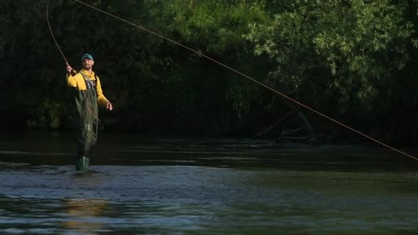 Человек рыбак держит удочку, бросает поплавок, рыбачит в реке — стоковое видео