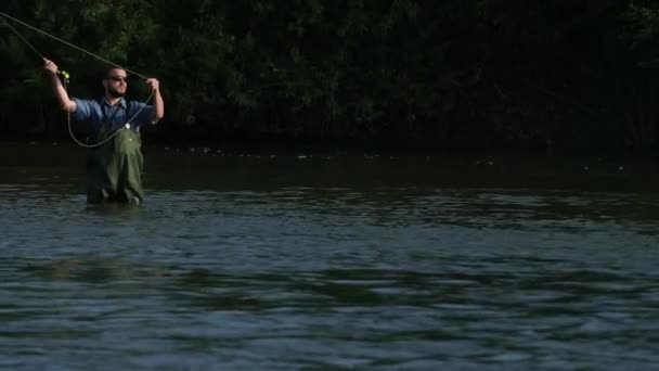 Άνθρωπος ψαράς που κρατά ένα καλάμι ψαρέματος, πετάει ένα άρμα, ψαρεύει στο ποτάμι — Αρχείο Βίντεο