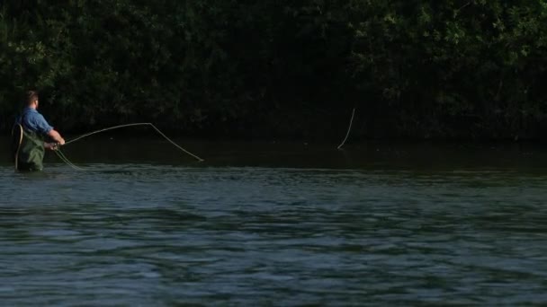 Man fiskare som innehar ett fiskespö, kastar en flottör, fiske i floden — Stockvideo