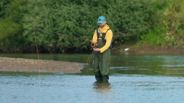 Человек рыбак держит удочку, бросает поплавок, рыбачит в реке — стоковое видео
