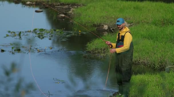 Uomo pescatore in possesso di una canna da pesca, getta un galleggiante, pesca nel fiume — Video Stock