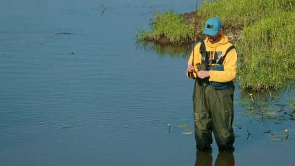 Uomo pescatore in possesso di una canna da pesca, getta un galleggiante, pesca nel fiume — Video Stock