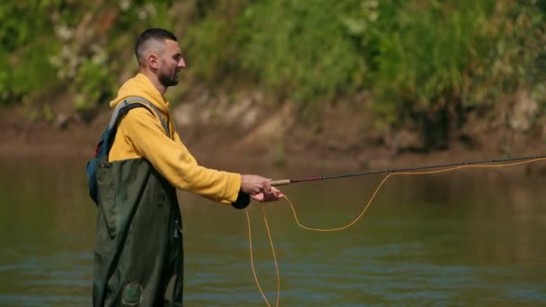 Pescador macho lanza una carroza, pesca en el río, de pie en el agua — Vídeo de stock