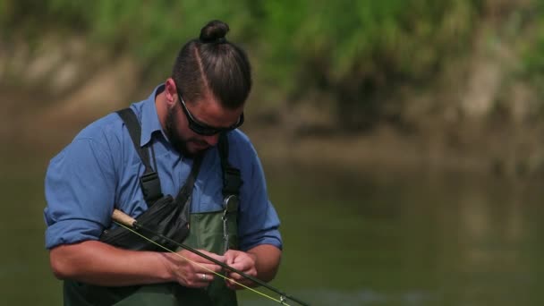 Fischer, der eine Angelrute in der Hand hält, Köder anlegt, auf dem Fluss, im Wasser stehend — Stockvideo