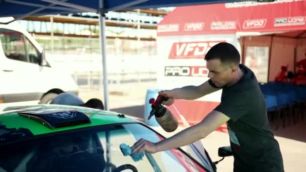 Νέος άντρας πλένει το παρμπρίζ ενός πράσινου αθλητικού αυτοκινήτου για τη μετατόπιση του δρόμου — Αρχείο Βίντεο
