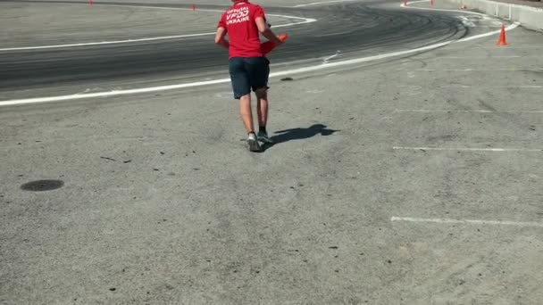 Homem em uma t-shirt vermelha corre e endireita chips laranja ao longo da pista — Vídeo de Stock