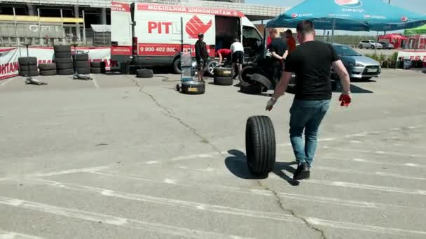 Hombre lleva un neumático, en la zona donde hay una gran cantidad de coches de carreras deportivas — Vídeos de Stock