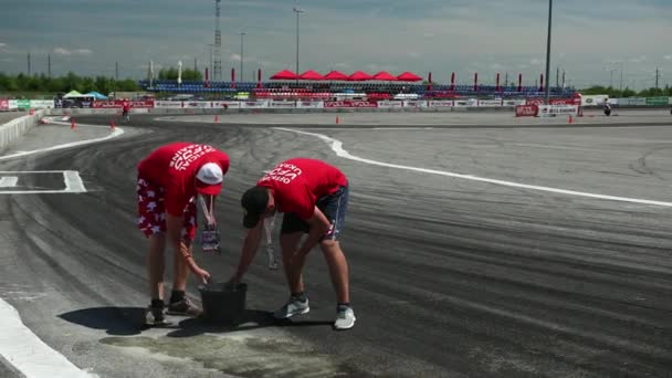 Dwóch mężczyzn posypać piasek na miejscu toru rozlane oleju, na którym znajdują się samochody sportowe — Wideo stockowe