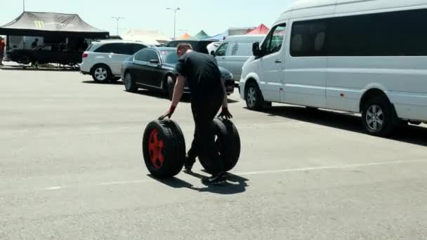 Man rolt twee wielen met oranje schijven, waar er veel auto's — Stockvideo