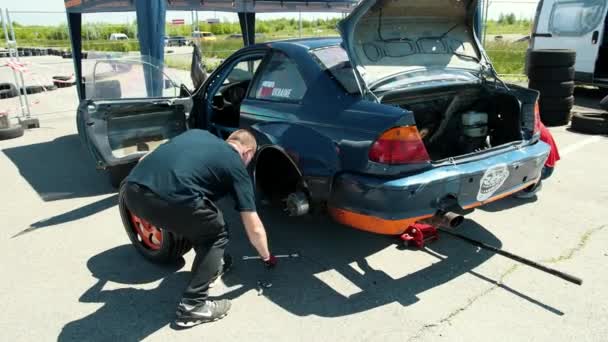 Νέος άνθρωπος εισάγει τροχό με ένα πορτοκαλί δίσκο σε ένα μπλε σπορ αυτοκίνητο για αγωνιστικά — Αρχείο Βίντεο