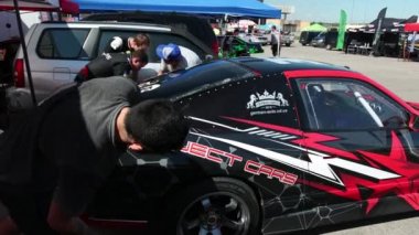 birçok genç insan kırmızı yarış spor araba, kaplama çıkartmaları yakınında duruyor