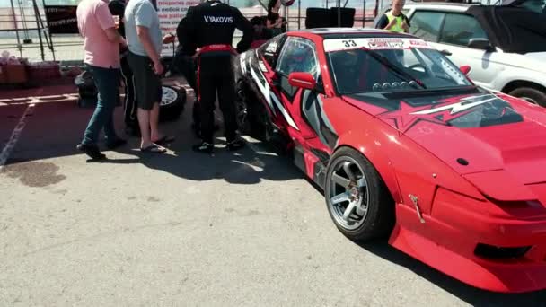 Muchos jóvenes están de pie cerca del coche deportivo de carreras rojas, pegatinas de chapa — Vídeo de stock